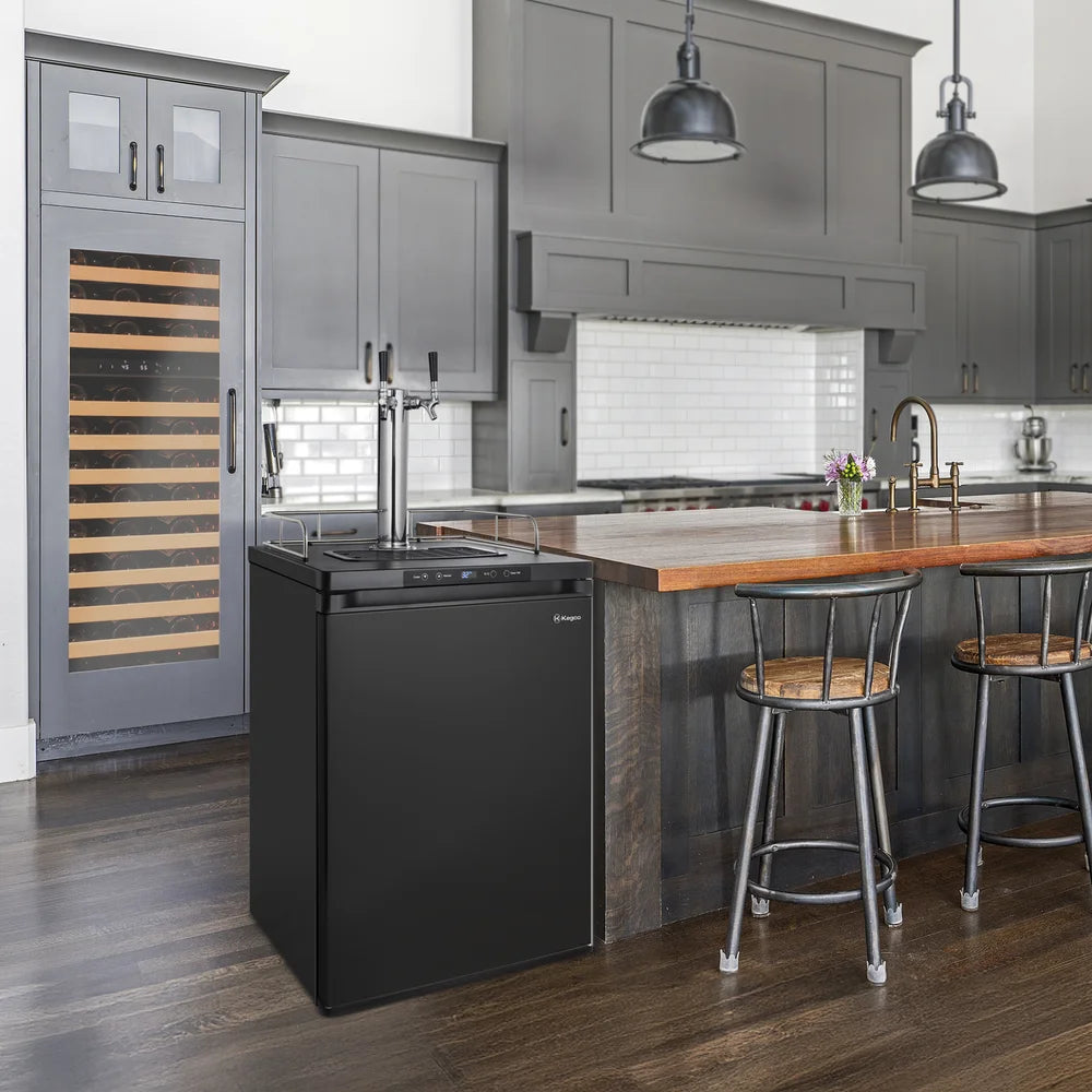 Black Kegco K309 Kegerator tucked beside a wood-topped kitchen island with bar stools and grey cabinets